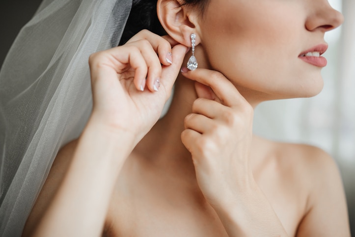 Wedding preparation. Beautiful, happy bride dresses earrings before wedding. Wedding accessories, jewelry. Closeup portrait of bride. Selective focus.