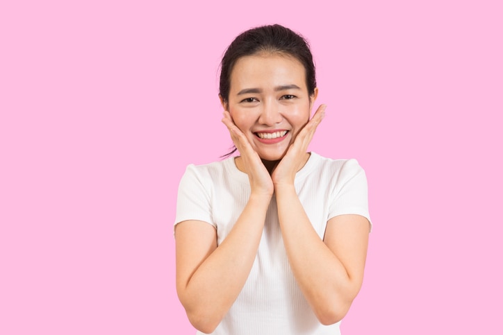 Cute asian presenting her face with hands touching face in v shape, portrait, skincare and cosmetic concept, white shirt, pink background