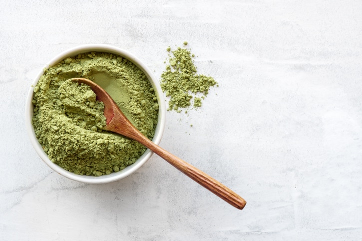 Matcha tea powder with spoon on white concrete background with copy space.