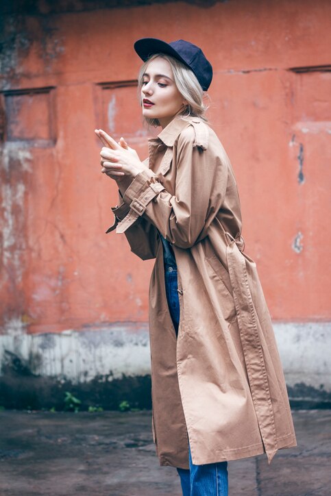 A young beautiful blonde woman is walking and enjoying small urban street in Shanghai. She is wearing nice long brown coat and black hat. Her gorgeous face is accentuated by a dark red lipstick.