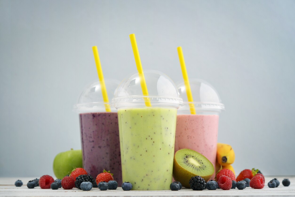 Fruit smoothies in plastic cups with blueberry, strawberry, kiwi, blackberry, raspberry and banana on blue background. Take away drinks 