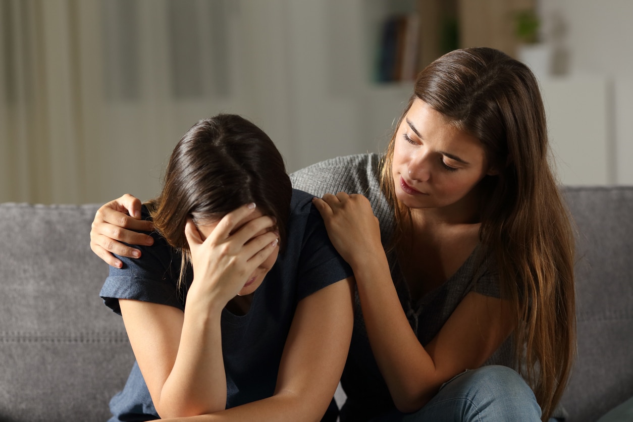 Teen comforting hes sad friend in the night sitting on a couch in the living room at home