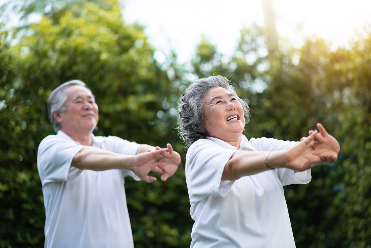 Happy Asian senior couple stretching hands before exercise at park outdoor. Smiling People in white shirts.