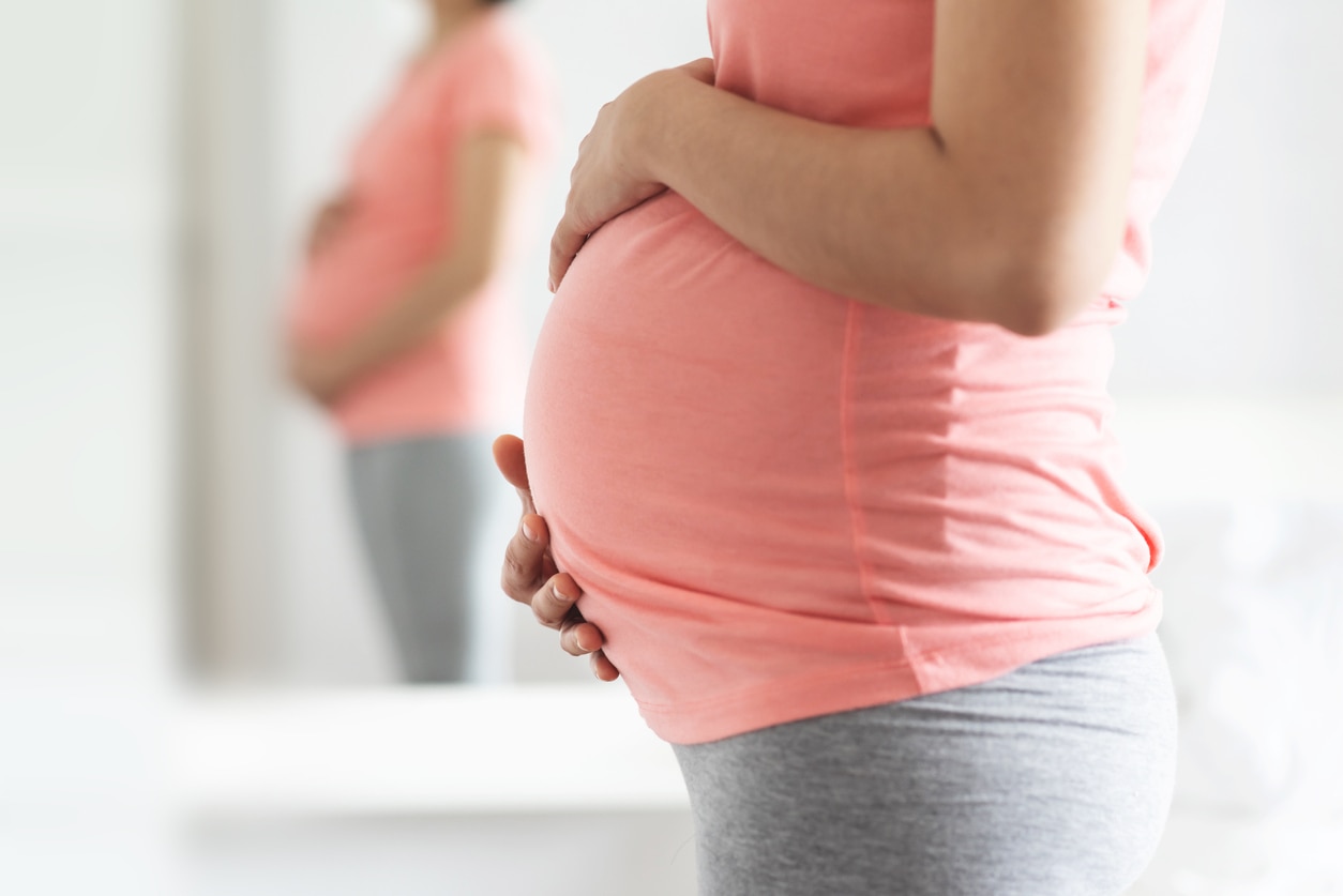 Pregnancy can cause a UTI. Close-Up Pregnant Woman in pink shirt standing touching her belly with copy space. 